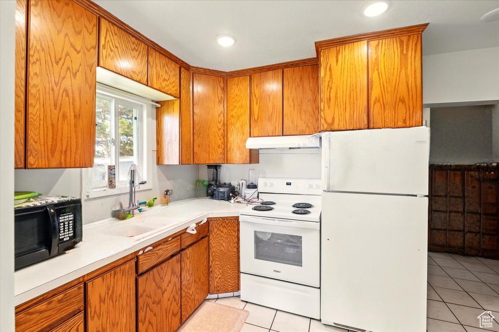Kitchen with white appliances, under cabinet range hood, a sink, light tile patterned floors, and light countertops