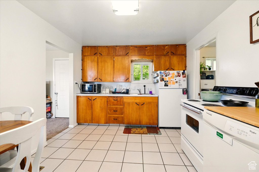 Kitchen featuring white appliances, brown cabinets, light countertops, and a sink