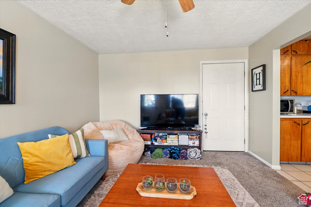 Living room featuring ceiling fan, light carpet, a textured ceiling, and light tile patterned floors