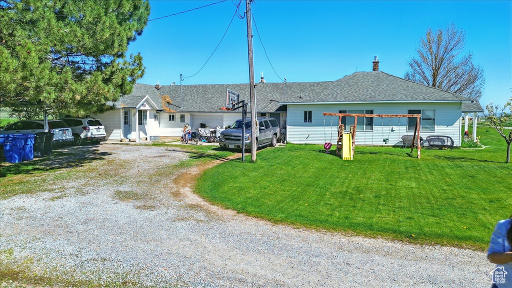 View of front of property with a front lawn, dirt driveway, and roof with shingles