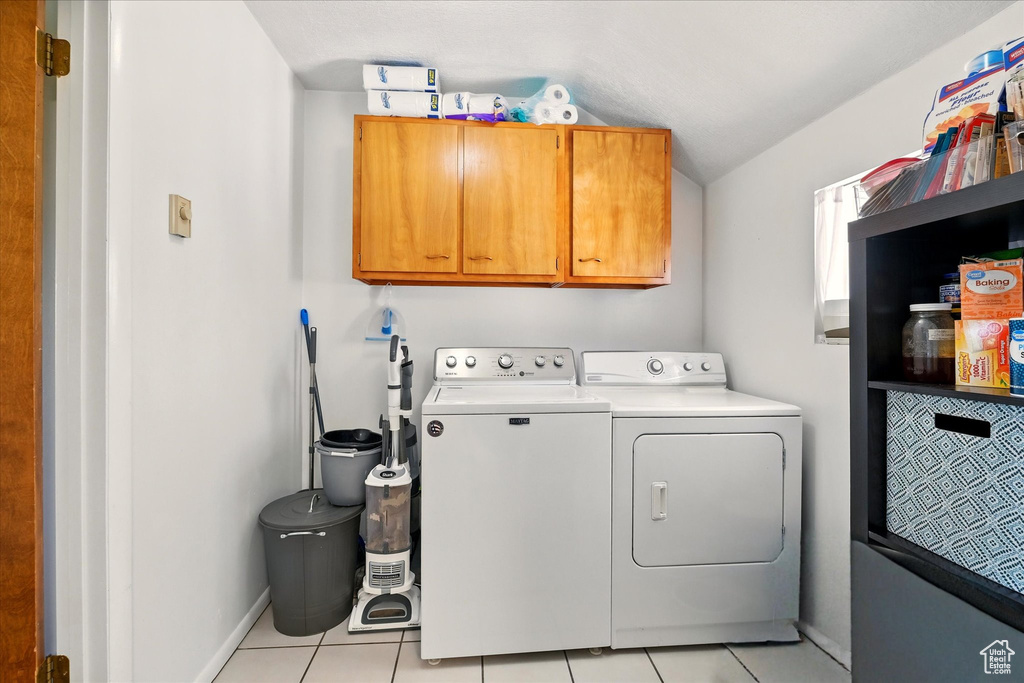 Washroom featuring washing machine and clothes dryer, cabinet space, light tile patterned floors, and baseboards