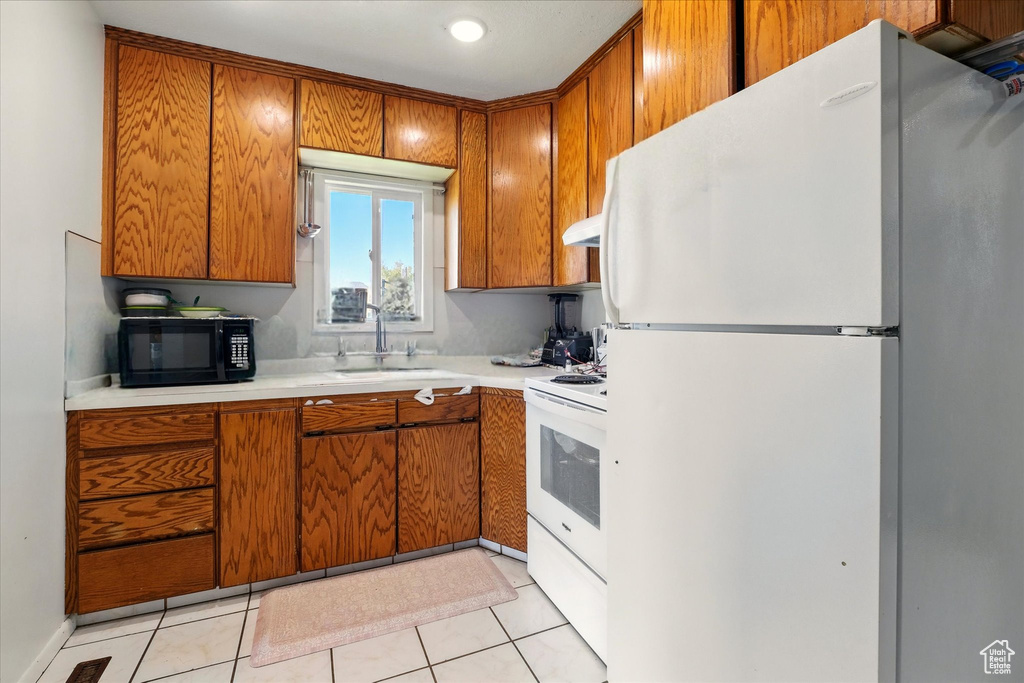 Kitchen featuring white appliances, a sink, brown cabinets, and light countertops