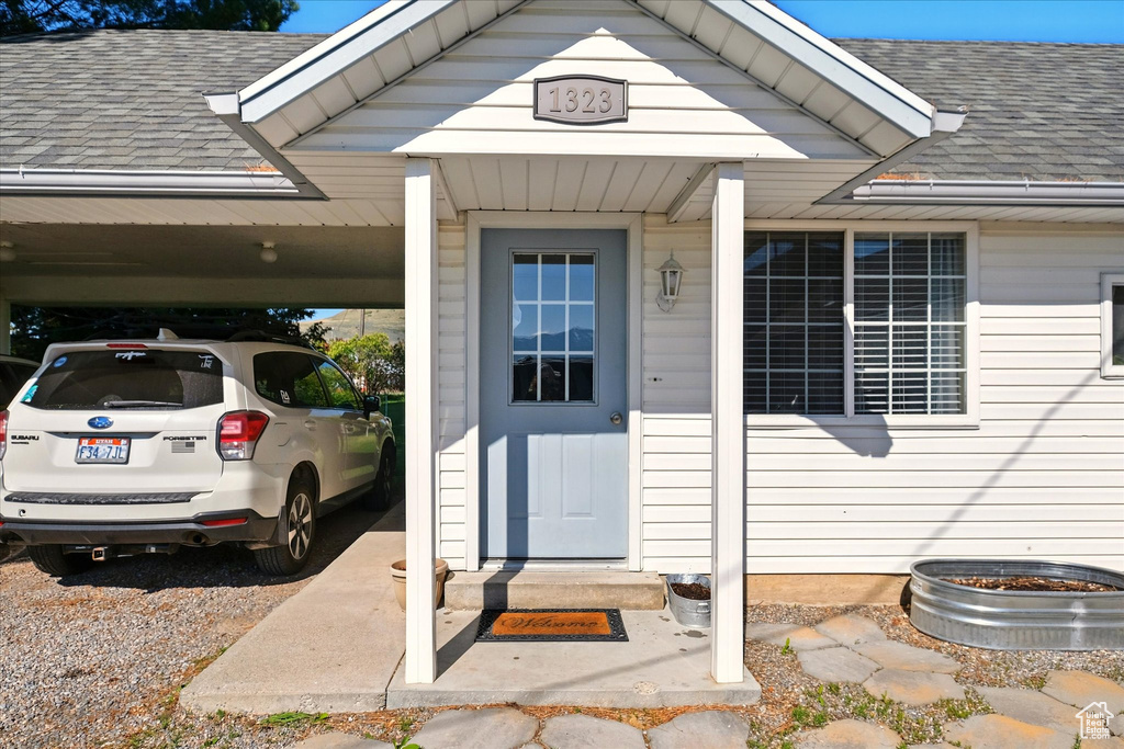 Entrance to property featuring a shingled roof and an attached carport