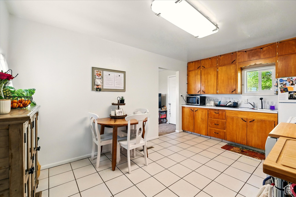Kitchen featuring freestanding refrigerator, stainless steel microwave, light countertops, brown cabinets, and a sink