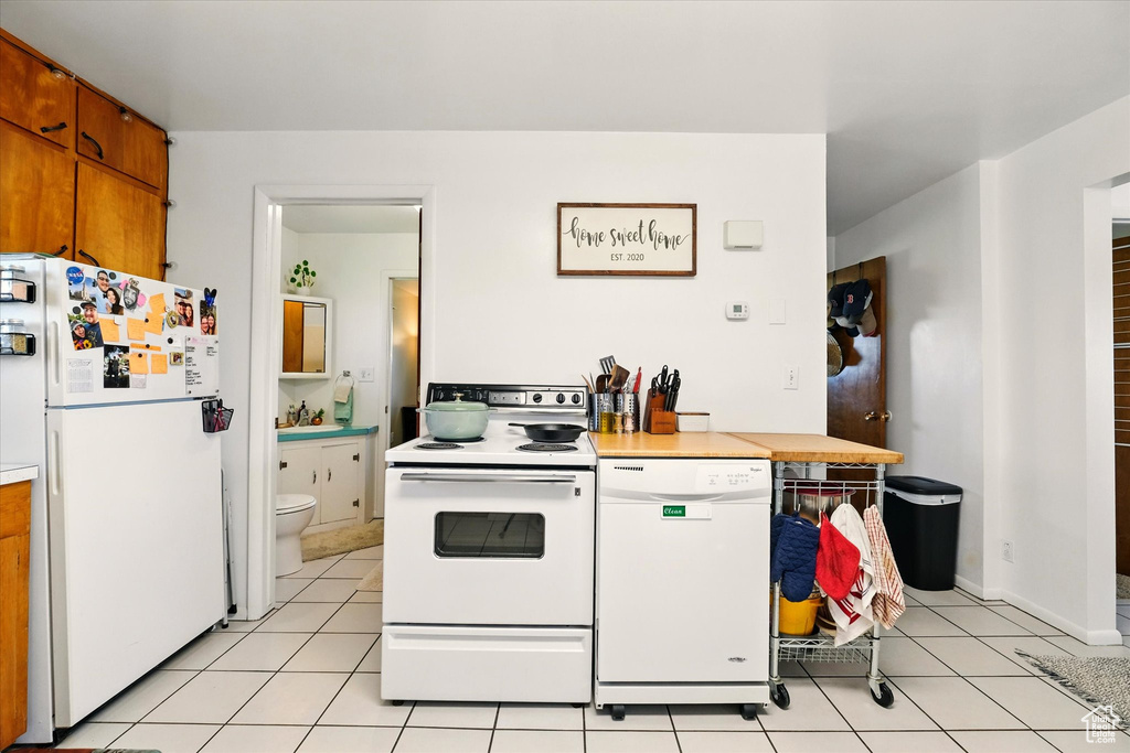 Kitchen with white appliances, brown cabinetry, light tile patterned floors, and light countertops