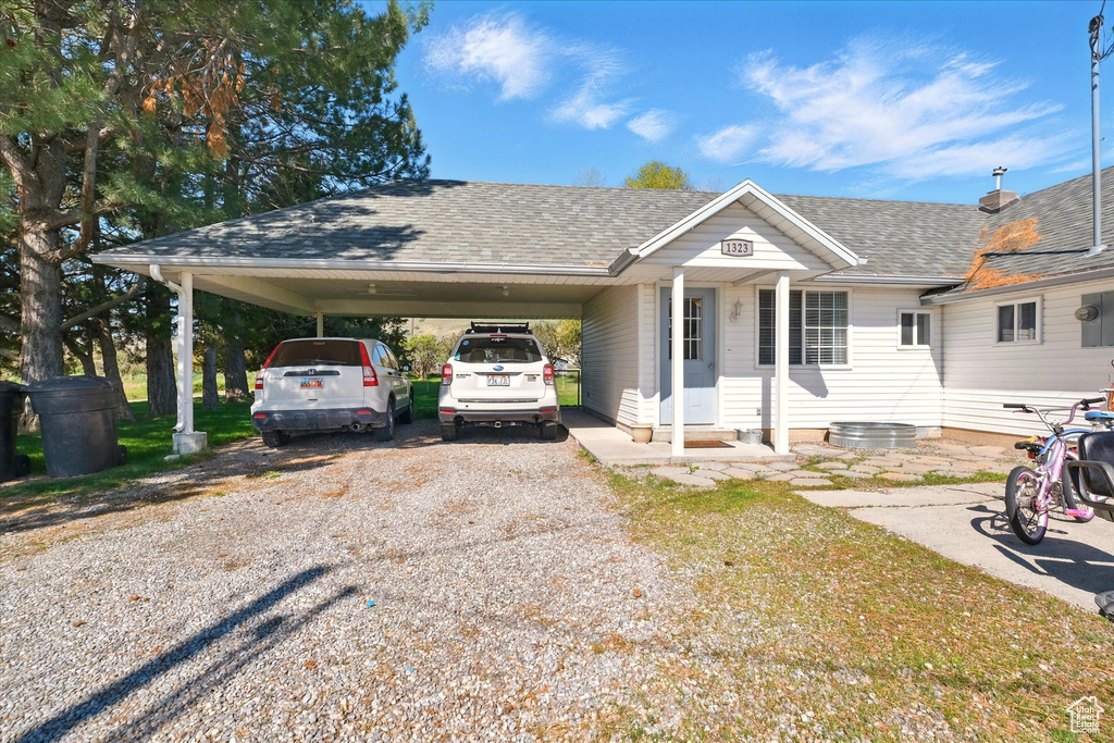 View of front facade featuring an attached carport, gravel driveway, and roof with shingles