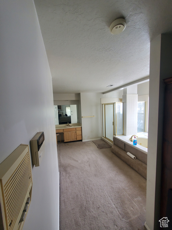 Full bathroom featuring a bath, a stall shower, a textured ceiling, baseboards, and a sink