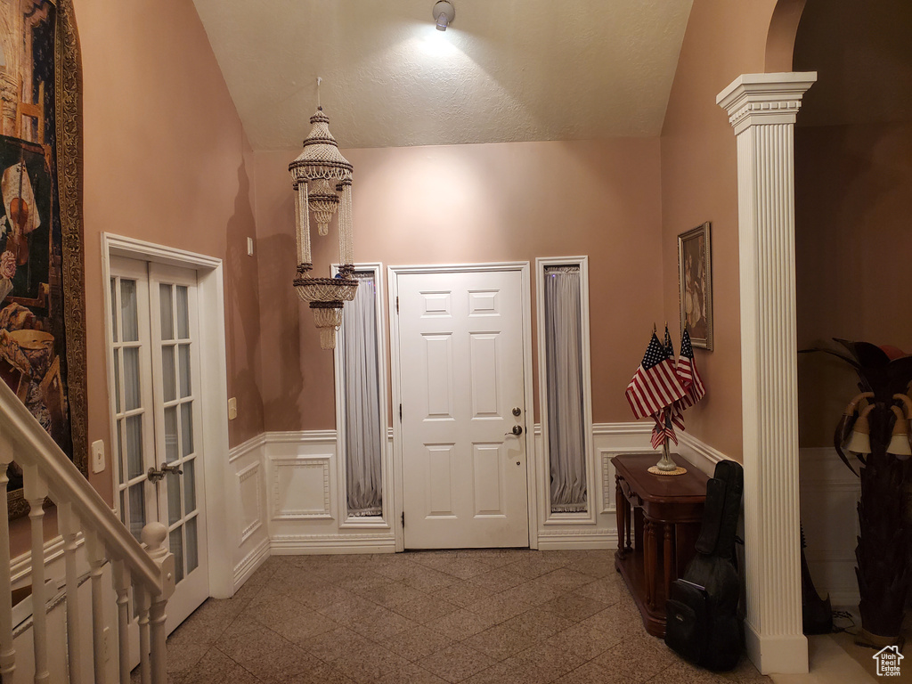 Entrance foyer featuring a decorative wall, a wainscoted wall, vaulted ceiling, and ornate columns