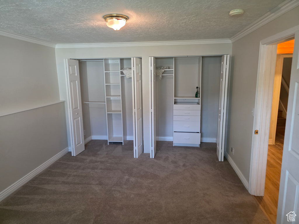 Unfurnished bedroom with two closets, a textured ceiling, carpet flooring, ornamental molding, and baseboards