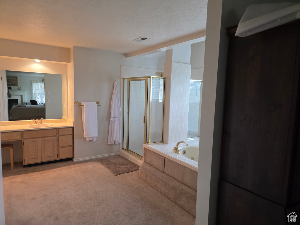 Full bath featuring ensuite bathroom, a shower stall, a tub with jets, vanity, and a textured ceiling