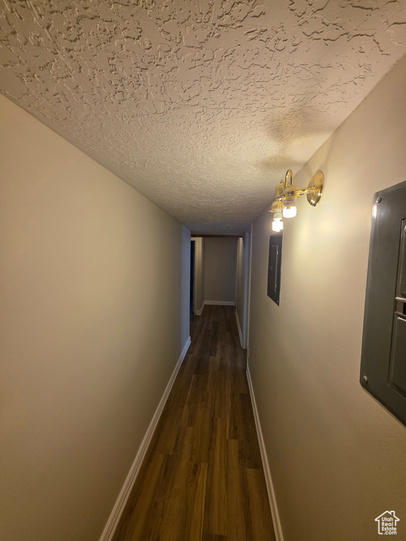Hallway featuring dark wood-type flooring, electric panel, baseboards, and a textured ceiling