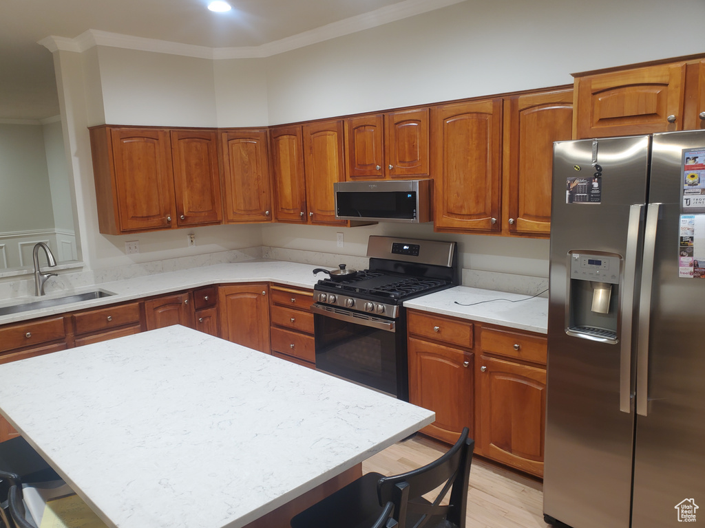 Kitchen featuring appliances with stainless steel finishes, a breakfast bar, a sink, ornamental molding, and brown cabinetry