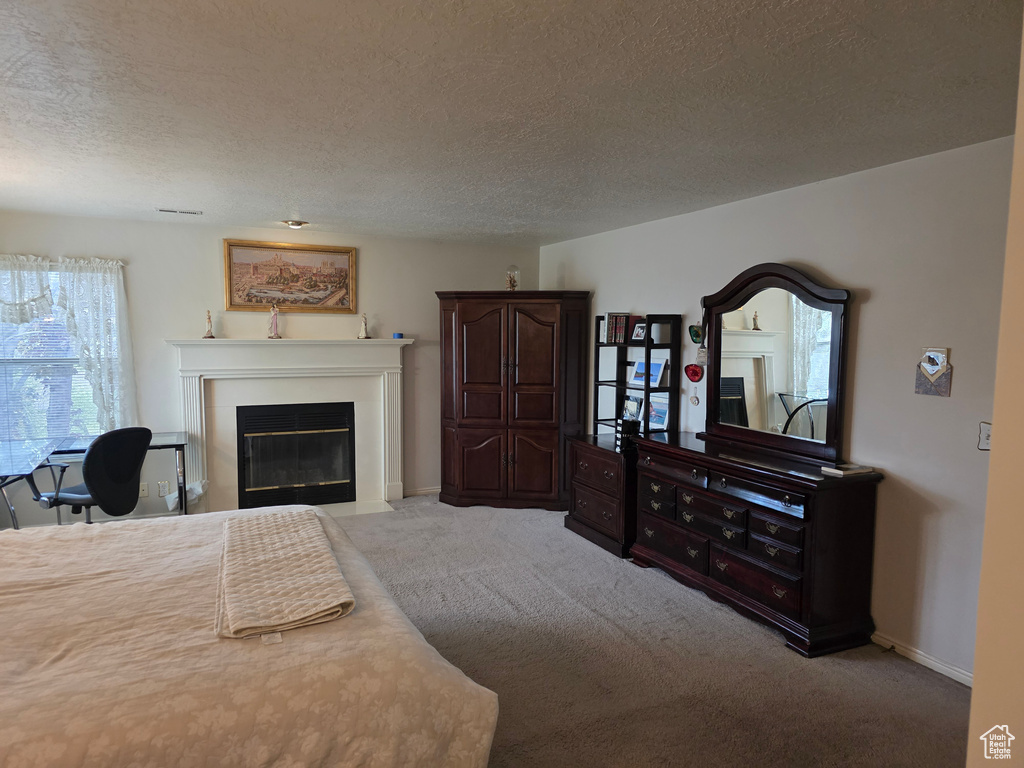 Carpeted bedroom with a textured ceiling, a fireplace with flush hearth, and baseboards
