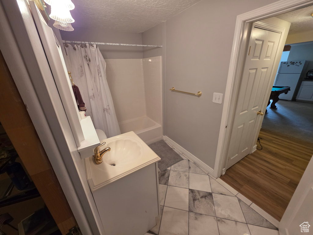 Bathroom with a textured ceiling, vanity, marble look tiles, shower / bath combo with shower curtain, and baseboards