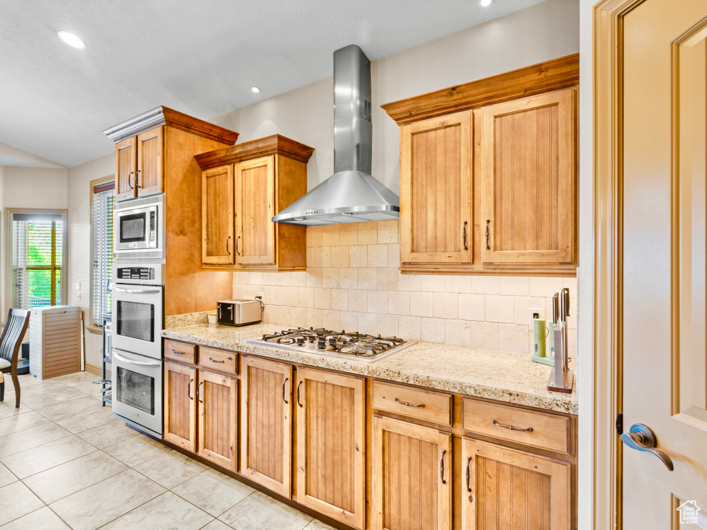 Kitchen with wall chimney range hood, double oven, stainless steel microwave, gas cooktop, and backsplash