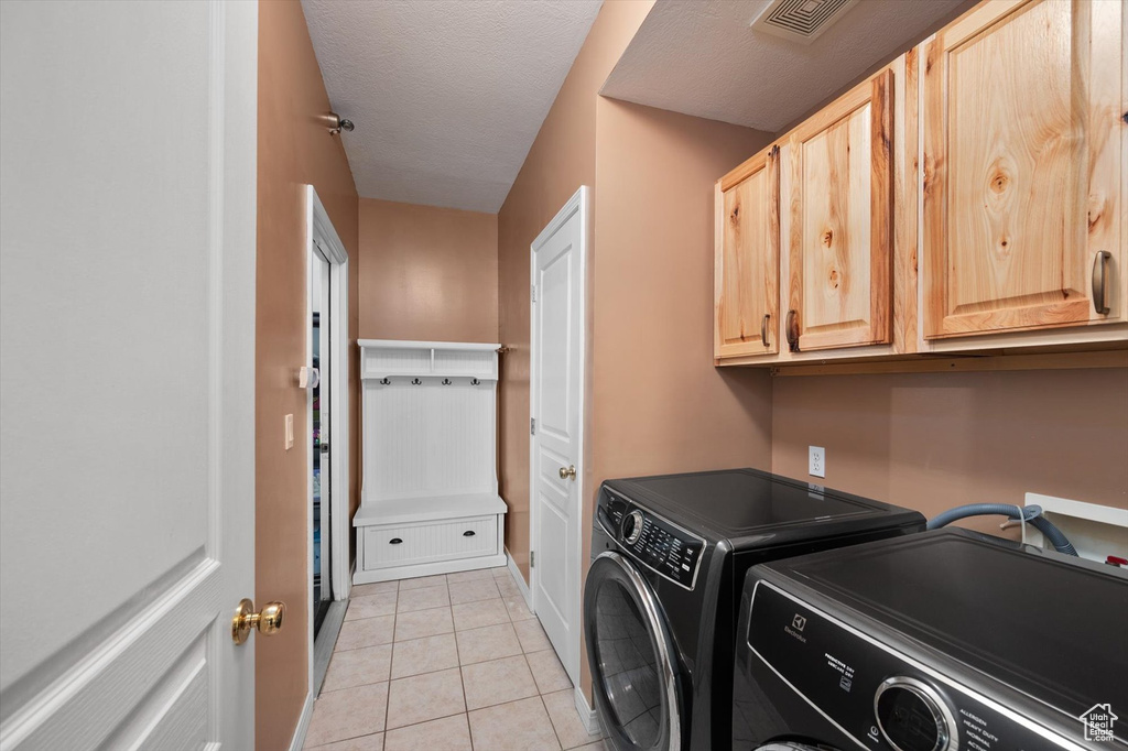Washroom with cabinet space, washer and dryer, light tile patterned floors, and baseboards