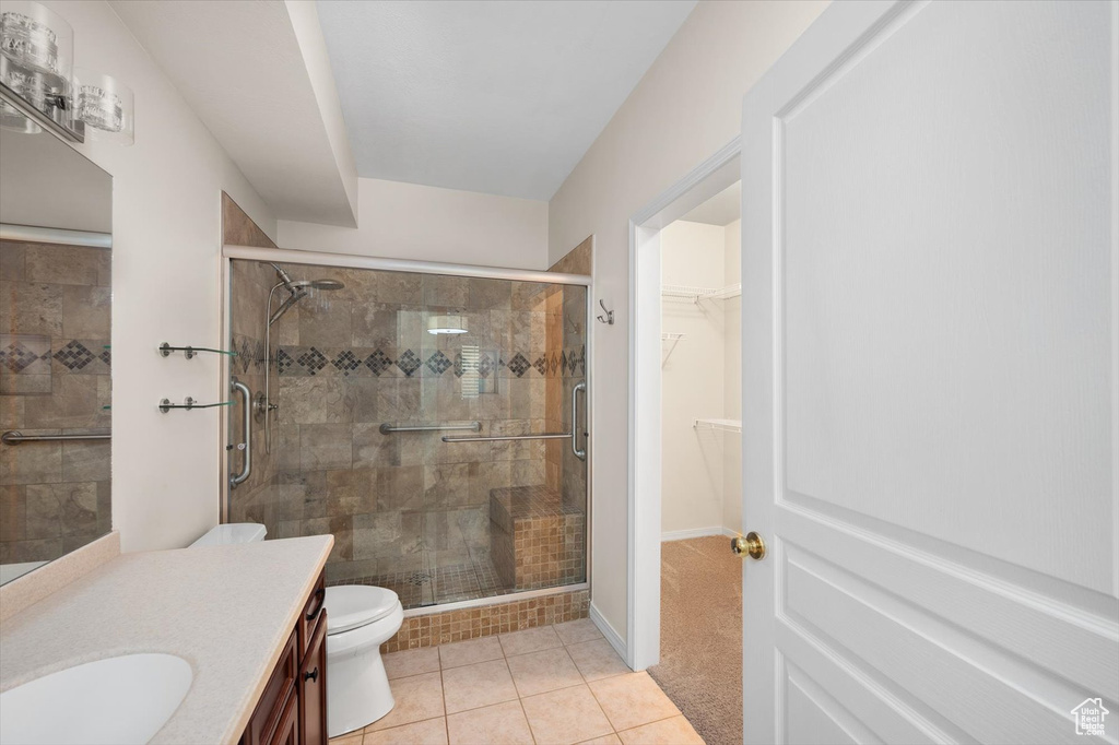 Bathroom with vanity, a shower stall, toilet, tile patterned floors, and a walk in closet