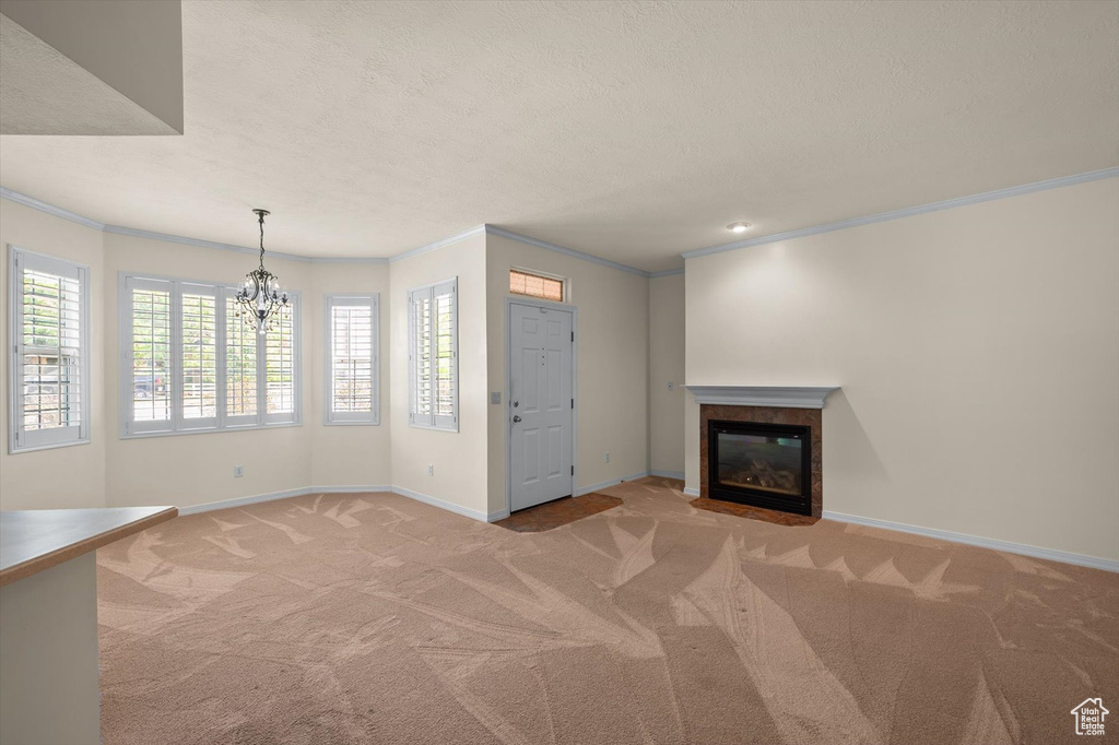 Unfurnished living room featuring light colored carpet, a fireplace, crown molding, a chandelier, and baseboards
