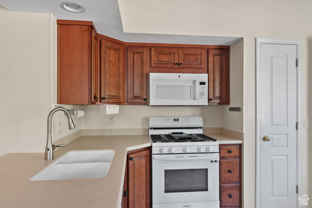 Kitchen with white appliances, a sink, light countertops, and brown cabinets