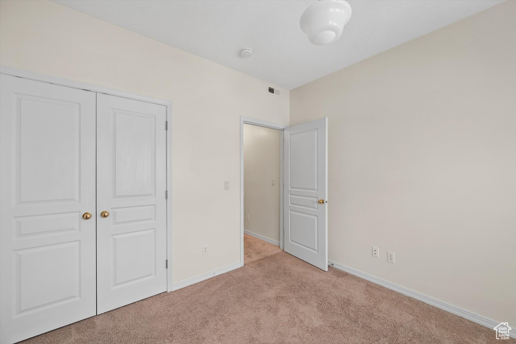 Unfurnished bedroom with light colored carpet, baseboards, and a closet