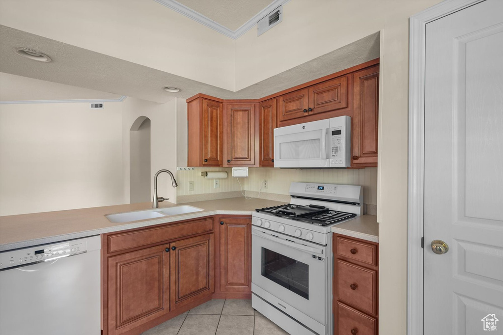 Kitchen featuring white appliances, a sink, brown cabinets, light countertops, and crown molding