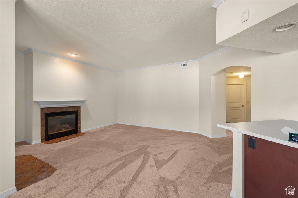 Unfurnished living room featuring light colored carpet, arched walkways, a tiled fireplace, crown molding, and baseboards