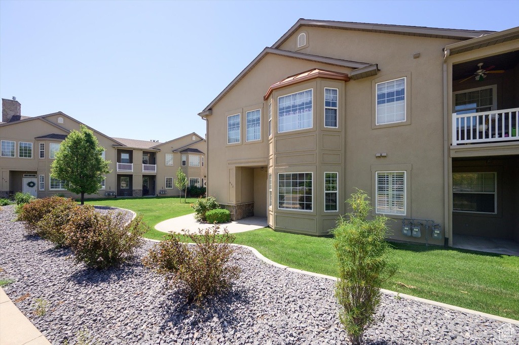 Rear view of property featuring stucco siding, a lawn, and ceiling fan