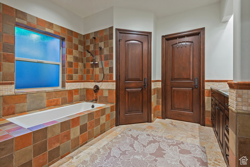 Full bath featuring tile walls, a wainscoted wall, tiled shower / bath, and vanity