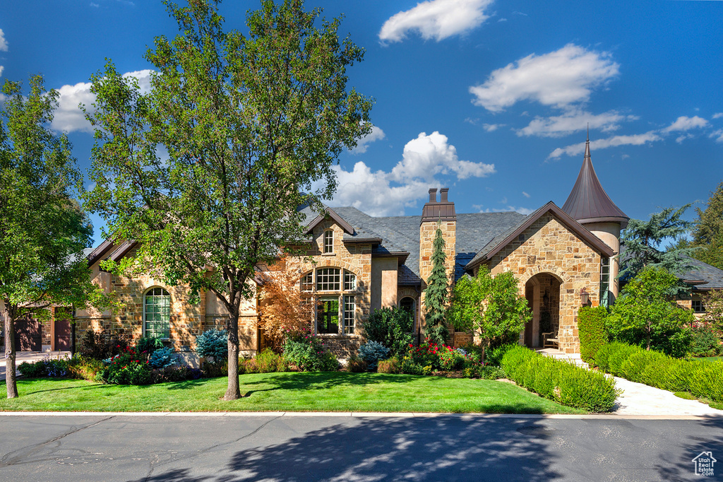 View of front of property with stone siding, a front yard, and a chimney