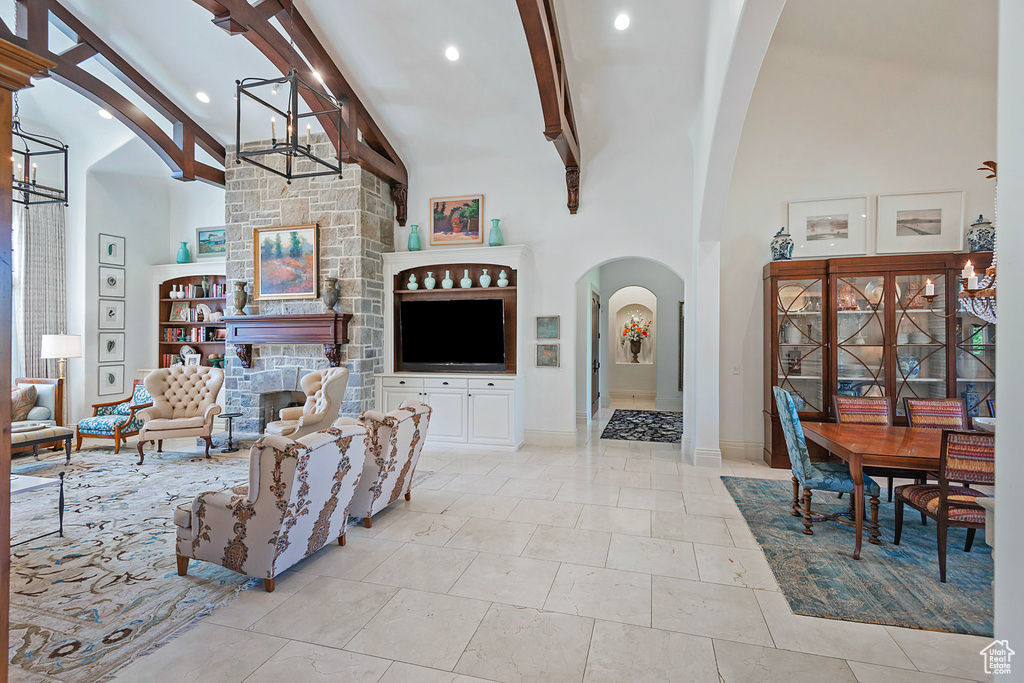 Living area with a chandelier, arched walkways, beamed ceiling, high vaulted ceiling, and a stone fireplace