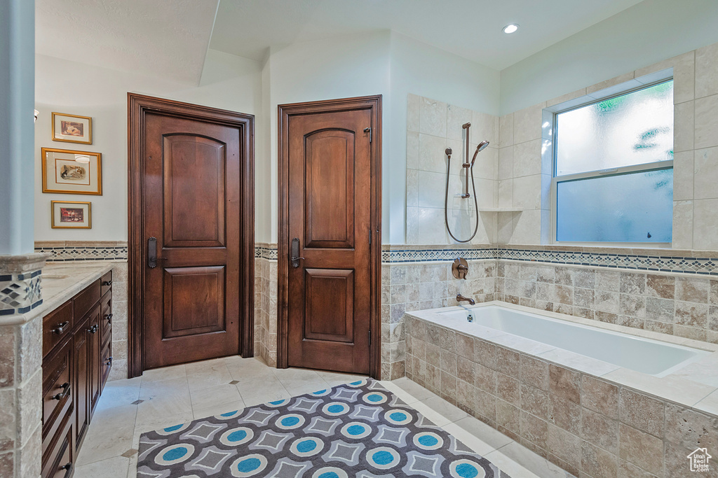 Full bath with tile walls, wainscoting, tile patterned flooring, tiled shower / bath combo, and vanity