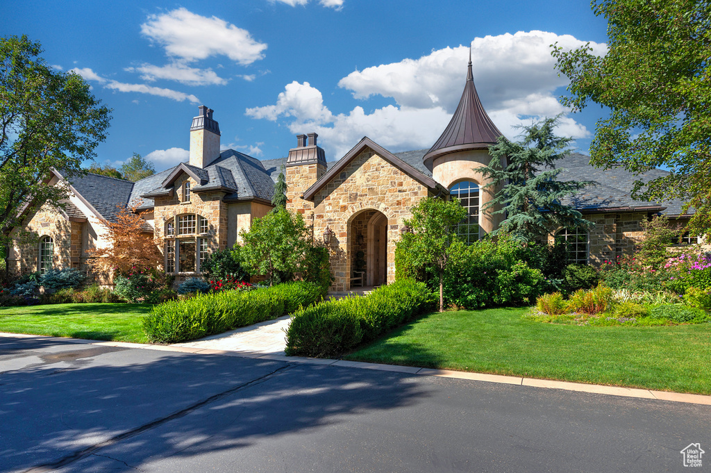 French provincial home with stone siding, a front yard, a chimney, and a high end roof
