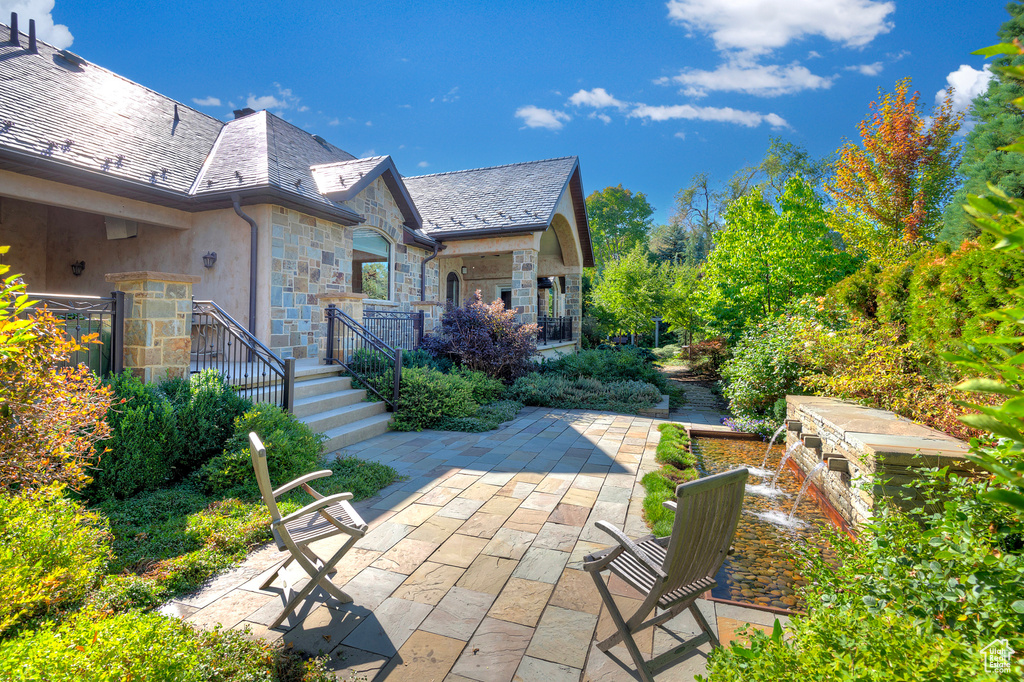 Rear view of house featuring stone siding, a patio, and a high end roof