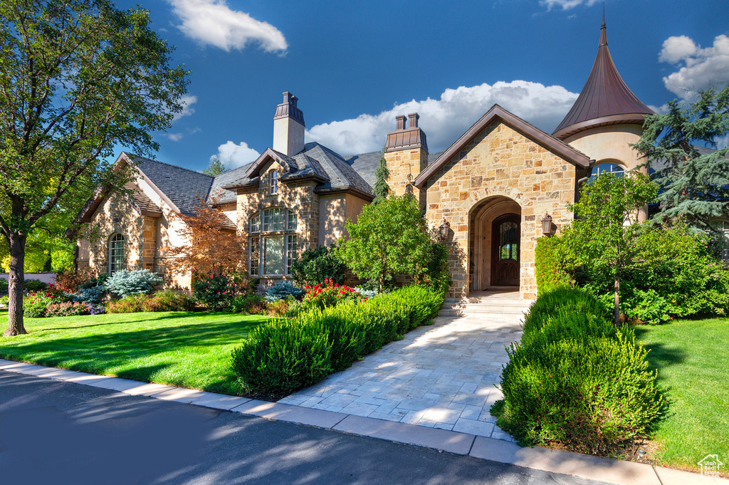 View of front of house featuring stone siding, a front lawn, a high end roof, and a chimney