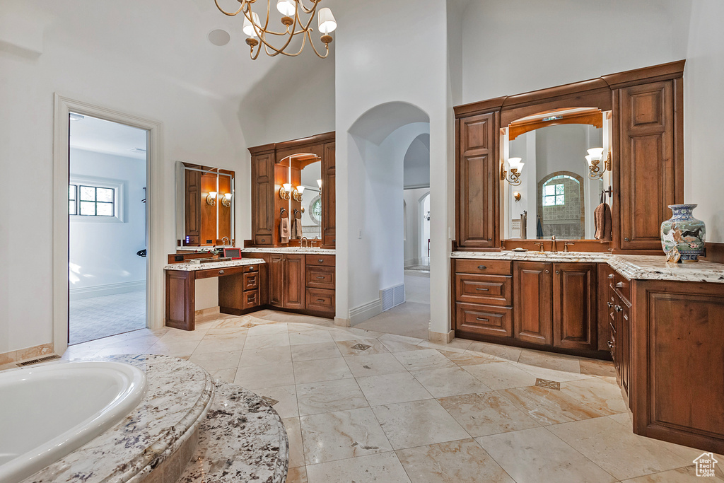 Bathroom featuring a chandelier, a high ceiling, a bath, baseboards, and two vanities