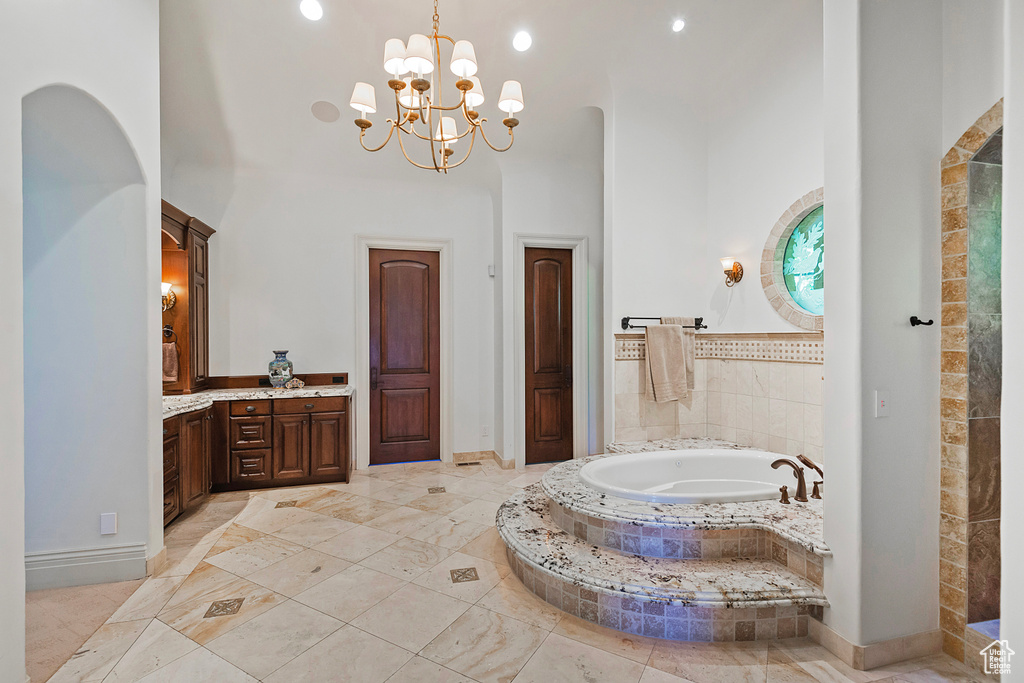 Full bathroom featuring a bath, a towering ceiling, vanity, a chandelier, and baseboards
