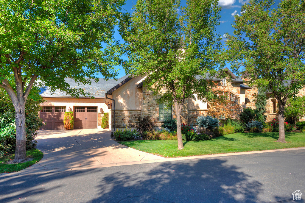 View of front of house with concrete driveway, stone siding, stucco siding, a front yard, and a garage