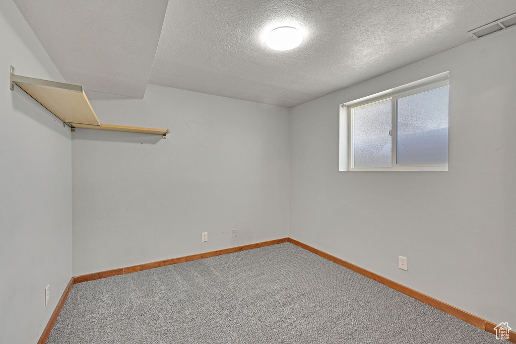 Empty room with a textured ceiling, carpet, and baseboards