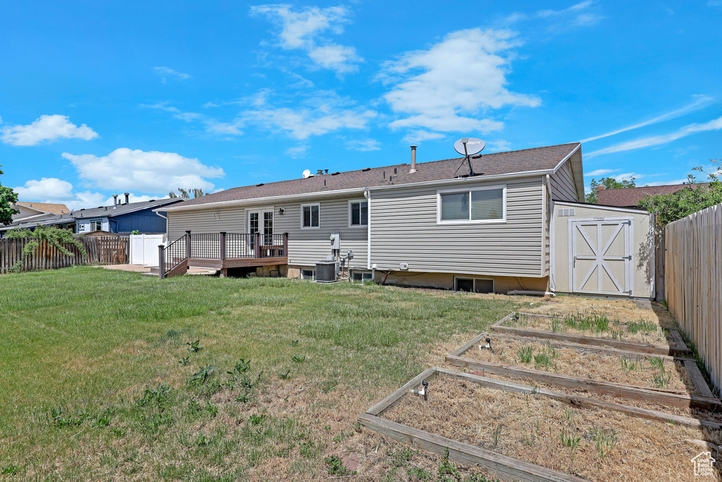 Rear view of house with a garden, a storage unit, a wooden deck, an outbuilding, and cooling unit