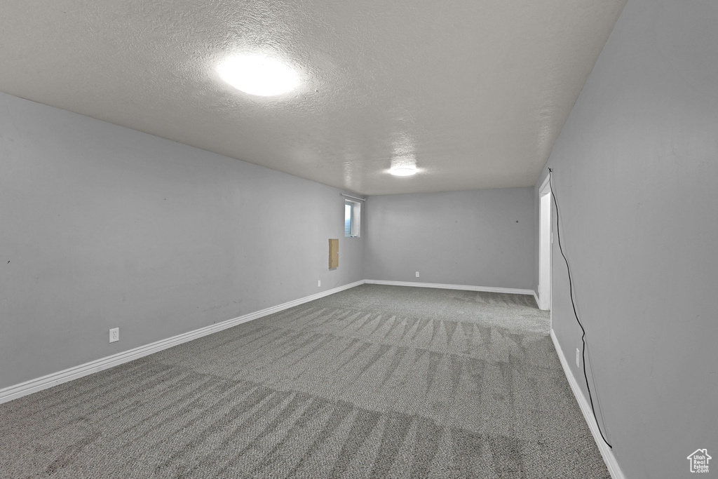 Carpeted empty room featuring a textured ceiling and baseboards
