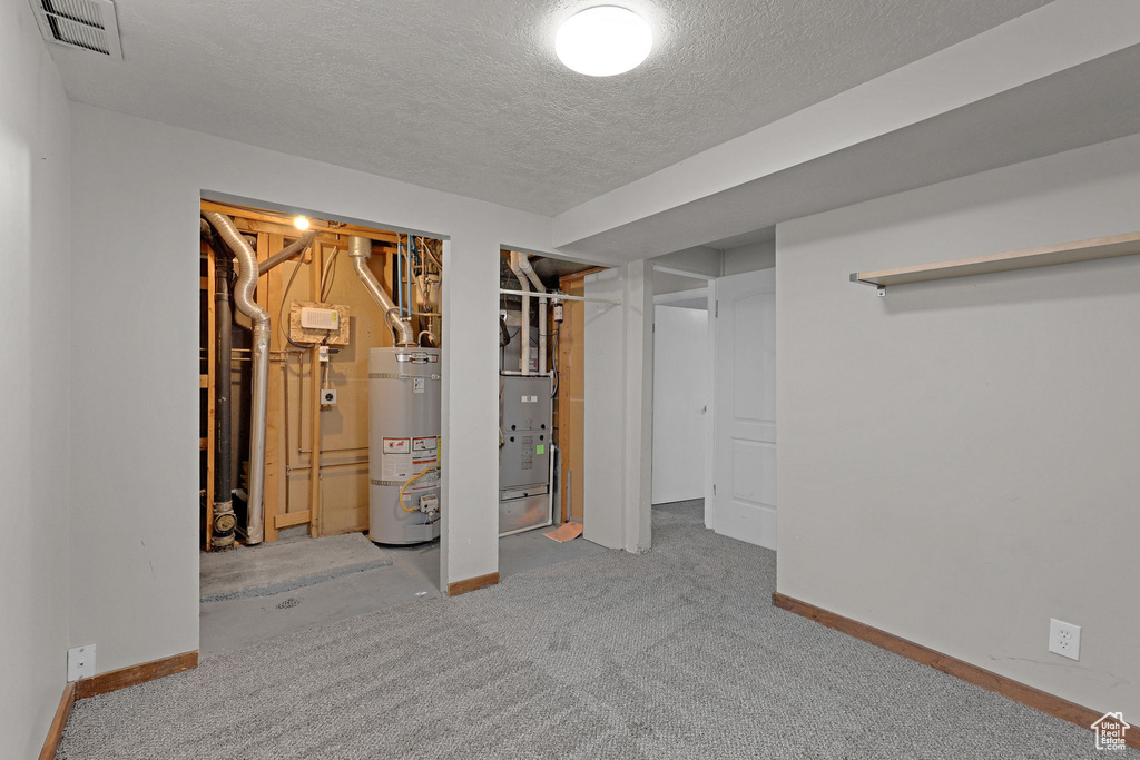 Finished below grade area with water heater, a textured ceiling, baseboards, and carpet
