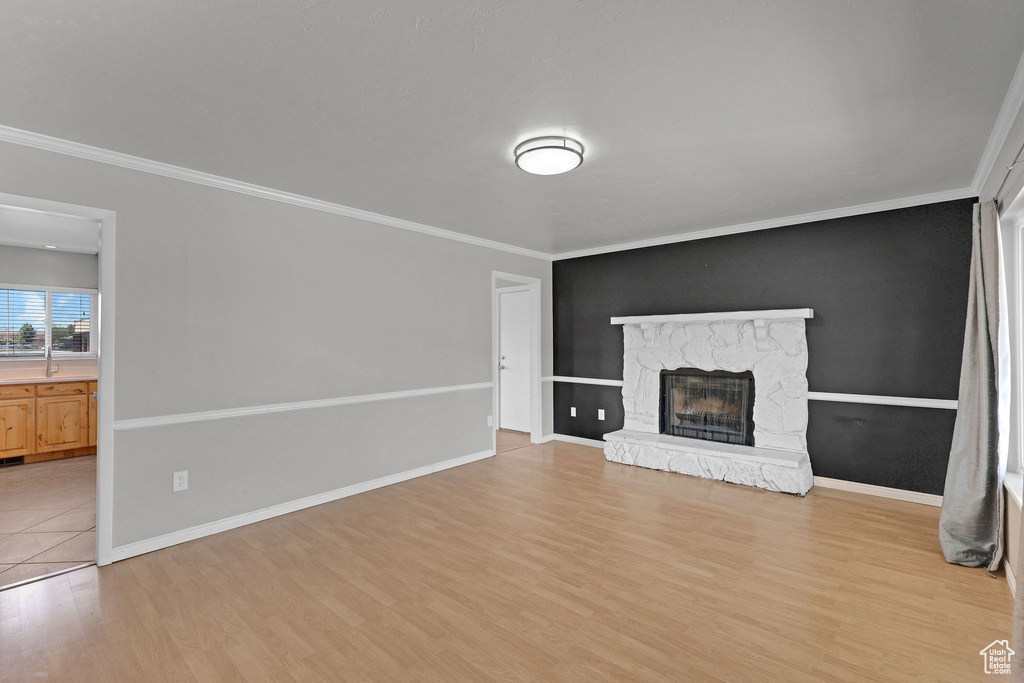 Unfurnished living room featuring light wood-type flooring, ornamental molding, a fireplace, baseboards, and a sink