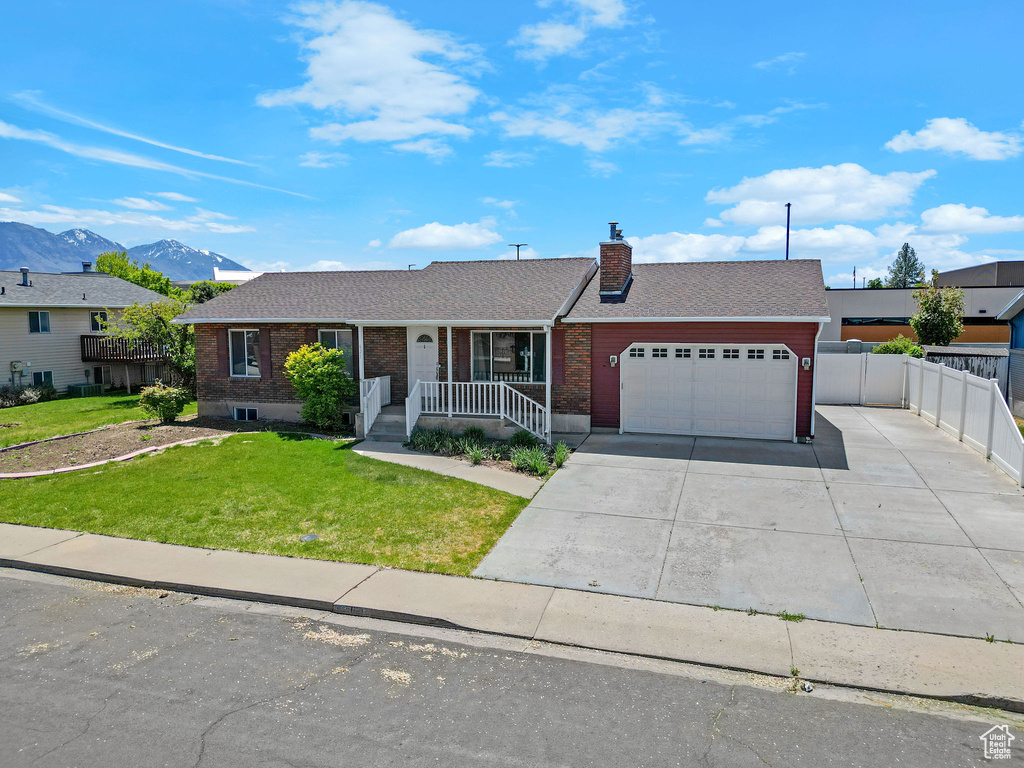 Single story home featuring a garage, concrete driveway, brick siding, a chimney, and a mountain view