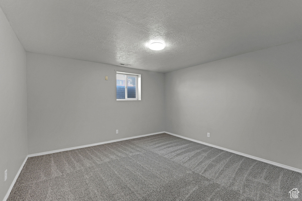 Empty room featuring a textured ceiling, baseboards, and dark carpet