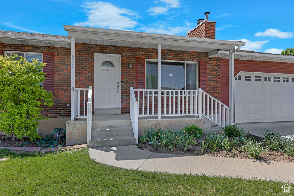 View of front of house with covered porch, an attached garage, brick siding, a chimney, and concrete driveway