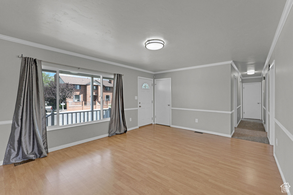 Unfurnished living room featuring wood finished floors, baseboards, and crown molding