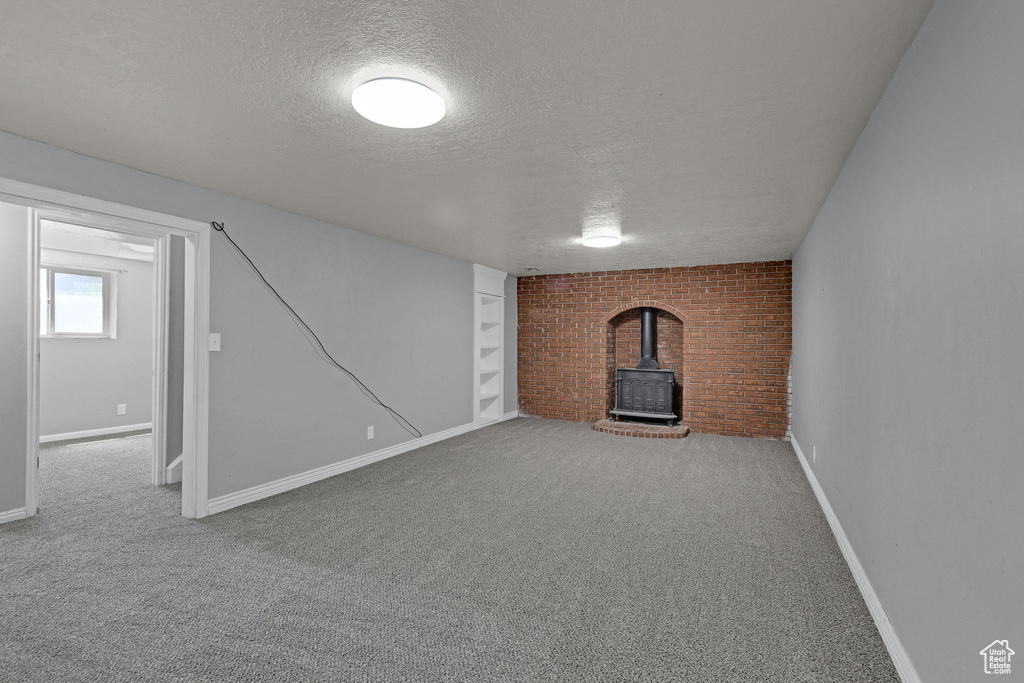 Basement with a wood stove, a textured ceiling, carpet floors, brick wall, and baseboards