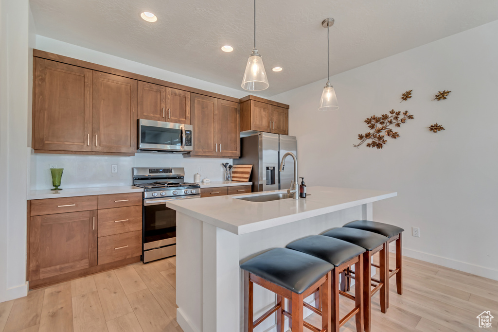 Kitchen featuring appliances with stainless steel finishes, a sink, light wood-style floors, a breakfast bar area, and recessed lighting