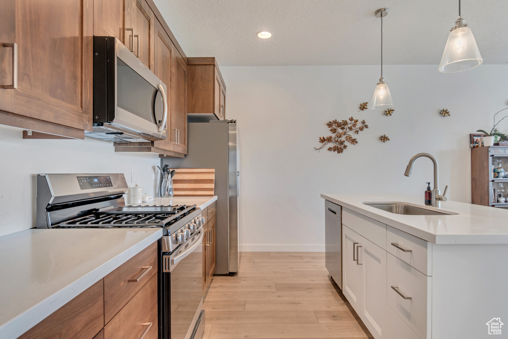 Kitchen with stainless steel appliances, a sink, light wood-style flooring, brown cabinetry, and light countertops