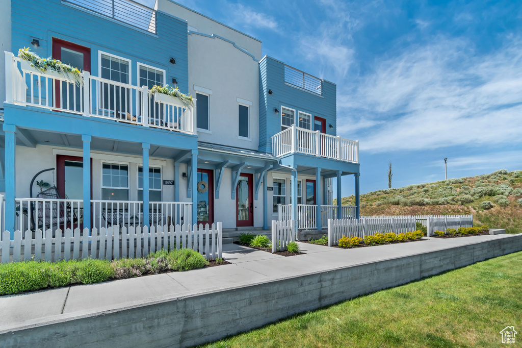 View of property featuring a balcony, covered porch, stucco siding, and a fenced front yard